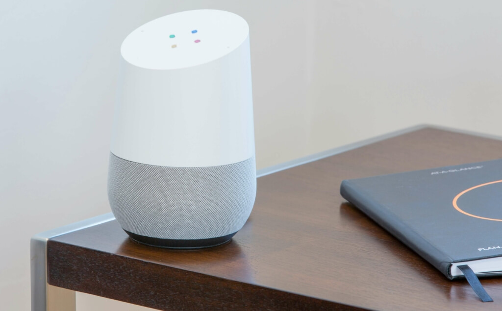 Google Home posé sur une table en bois dans un salon, permettant de contrôler le gainable multizones